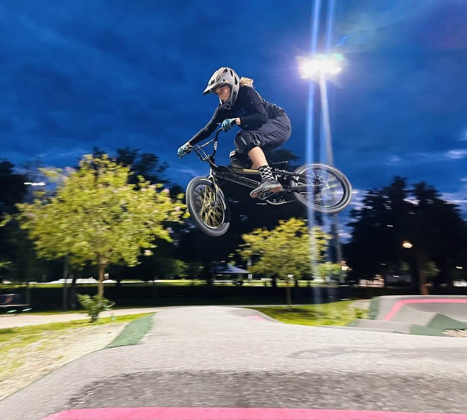 BMX rider Depler Bane catching air during a jump on an illuminated outdoor BMX track at twilight.
